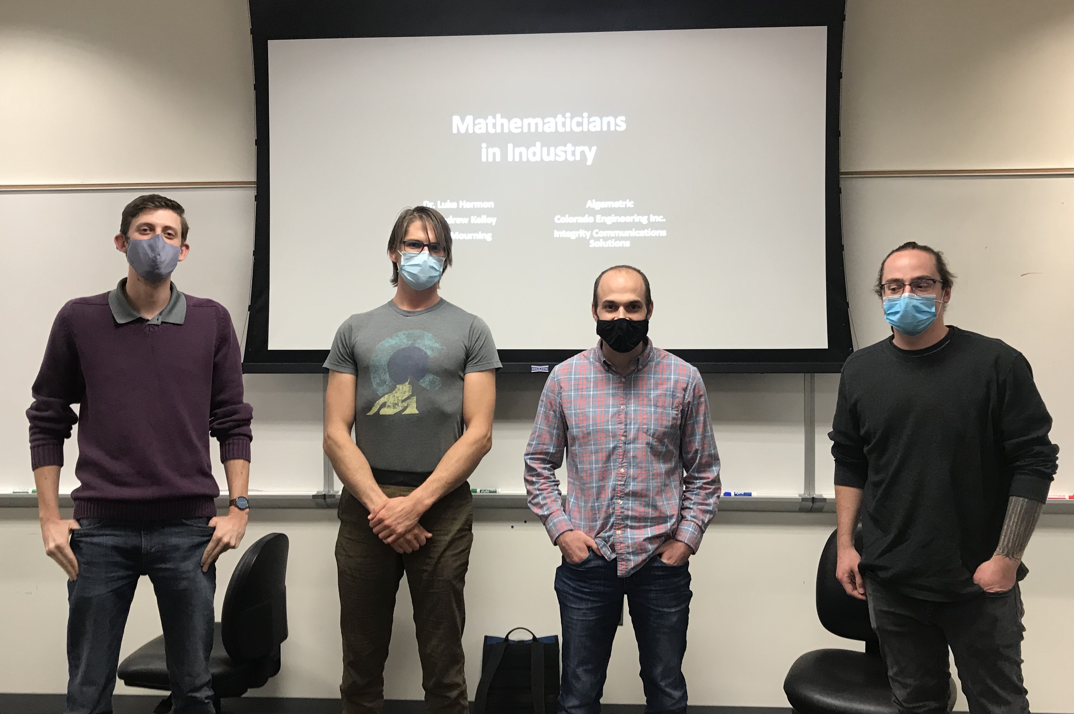 Four graduate students standing in front of a projection screen